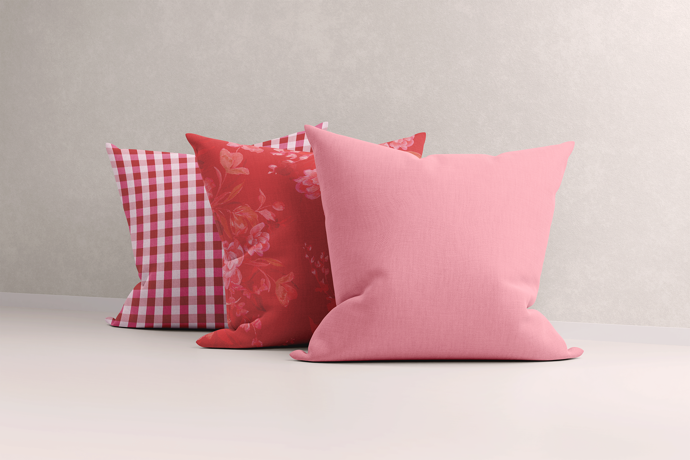 Trio of cushions against a plain backdrop featuring a bold red floral print, red gingham, and a pink cushion. The combination of red and pink hues creates a sophisticated feminine look, with vibrant, hand-painted designs that add a touch of joy and elegance to any space.